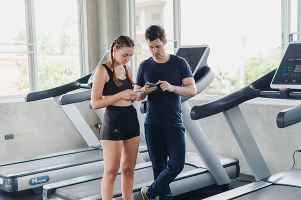 Couples exercise at the gym. Couple having fun playing with smartphones Near the exercise machine.