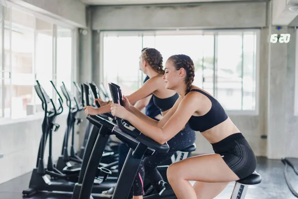 Bayan sporcular spor salonunda egzersiz yapmaktan, bisiklete binmekten bahsederler. Spor kıyafetleri giyerler..