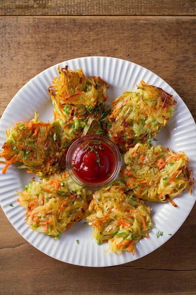 Potato Zucchini and Carrot Cakes. Vegetable fritters, latkes, draniki. Vegetable pancakes on white plate on wooden table. overhead, vertical