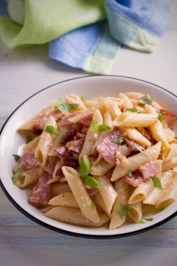 Pastırma ve güneşte kurutulmuş domates ile penne makarna. Alfredo penne makarna ahşap masa üzerinde beyaz tabakta. dikey