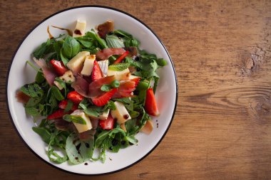 Çilek, fesleğen, nane, roka salatası brie peyniri ve jamon ahşap masa üzerinde beyaz tabakta. Yatay, ek yükü