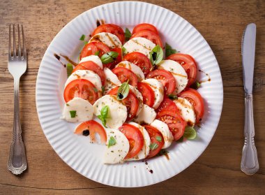 Domates, mozzarella peyniri, fesleğen, zeytinyağı ve beyaz tabakta balsamik sirke ile Caprese salatası. Tepegöz, yatay 