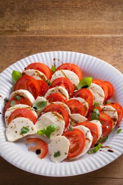 Domates, mozzarella peyniri, fesleğen, zeytinyağı ve beyaz tabakta balsamik sirke ile Caprese salatası. dikey