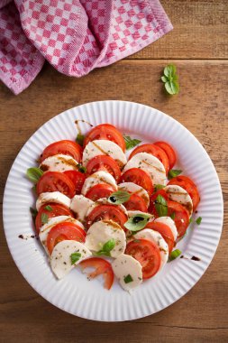 Domates, mozzarella peyniri, fesleğen, zeytinyağı ve beyaz tabakta balsamik sirke ile Caprese salatası. Tepegöz, dikey 