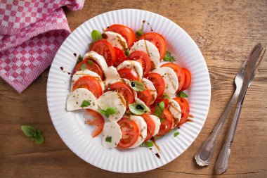 Domates, mozzarella peyniri, fesleğen, zeytinyağı ve beyaz tabakta balsamik sirke ile Caprese salatası. Tepegöz, yatay 