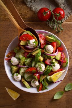 Avokado, domates, salatalık salatası ile mozzarella peyniri ahşap masa üzerinde beyaz kase. Tepegöz, dikey