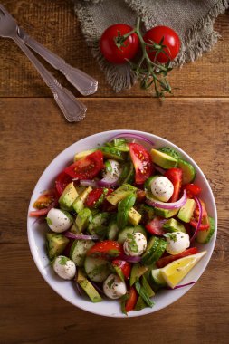 Avokado, domates, salatalık salatası ile mozzarella peyniri ahşap masa üzerinde beyaz kase. Tepegöz, dikey