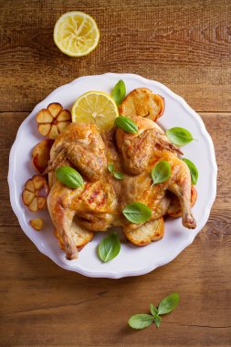 Bütün tavuk limon, fesleğen ve sarımsak beyaz plaka, ahşap masa üzerinde kızarmış ekmek üzerinde. Tepegöz, dikey