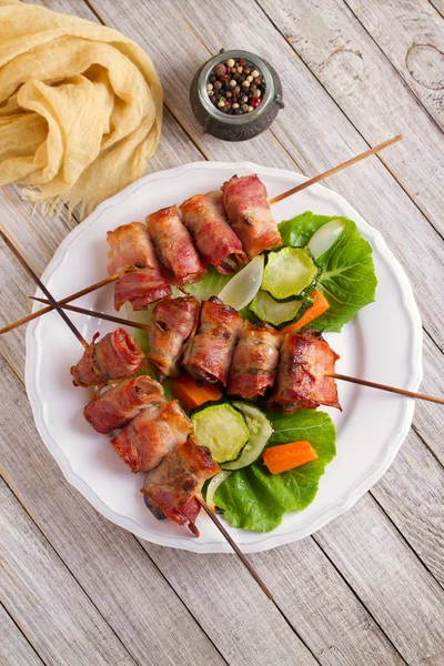 Chicken liver wrapped with bacon on skewers. Grilled liver kebabs with vegetables. View from above, top studio shot