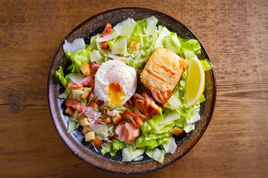 Somon Sezar salatası. Gevrek pan kızarmış somon fileto, pastırma, haşlanmış yumurta, marul ve kruton kase ahşap masa üzerinde. Tepegöz, yatay