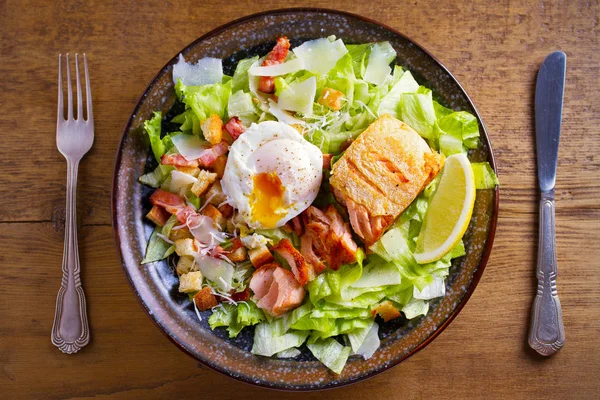 Salmon caesar salad. Crispy pan fried salmon fillet, bacon, poached egg, romaine lettuce and croutons in bowl on wooden table. overhead, horizontal