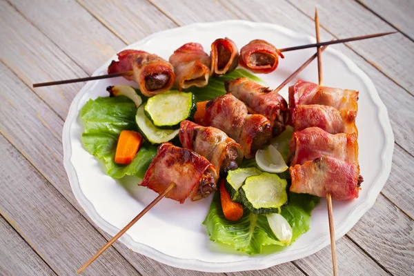 Chicken liver wrapped with bacon on skewers. Grilled liver kebabs with vegetables on white plate. horizontal