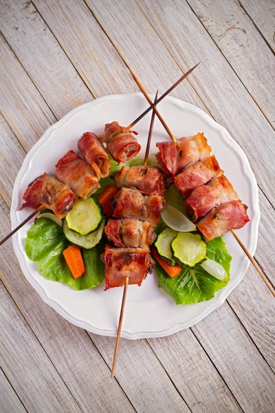 Chicken liver wrapped with bacon on skewers. Grilled liver kebabs with vegetables on white plate. overhead, vertical