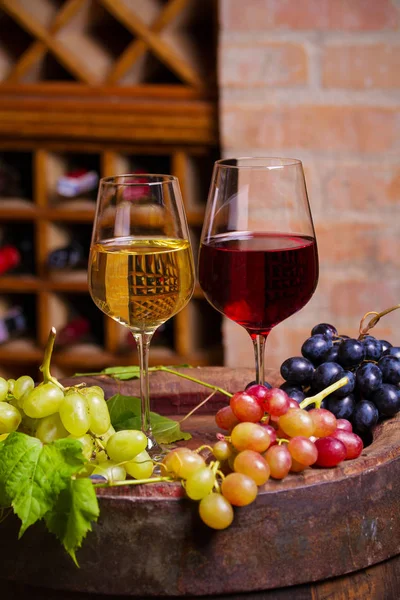 红酒窖里的老木桶上有葡萄的红白葡萄酒 酒杯和酒瓶 — 图库照片