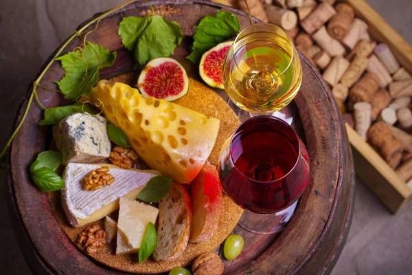 Red and white wine with cheese, grapes, figs and nuts on old cask in wine cellar. Glasses and bottles of wine. View from above, top studio shot