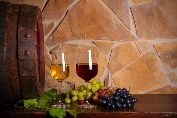 赤と白のワインはワインセラーで古樽の横にあるブドウ ガラスと木製のテーブルの上にワインのボトル 水平方向 — ストック写真