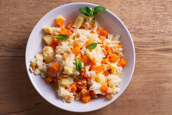 Rice porridge with pumpkin, apples and raisins in white bowl. Vegetarian diet dish of rice and pumpkin. Healthy food. overhead, horizontal