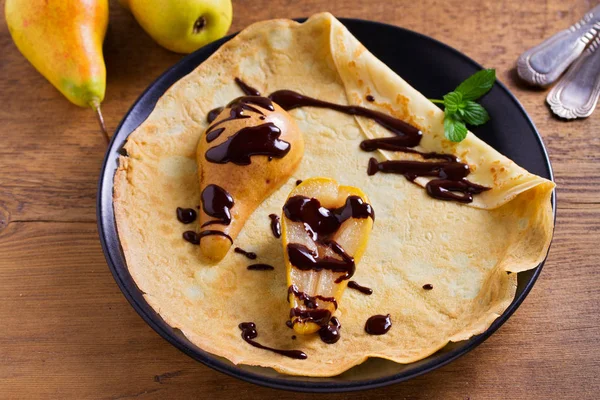 Crepes with baked pear and chocolate. Pancakes with baked pear and chocolate. View from above, top studio shot