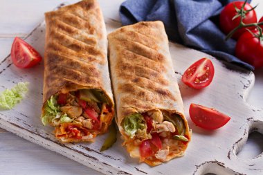 Tavuk domates, turşu, lahana ve soğan Beyaz Doğrama tahtası ve ahşap masa ile tamamladı. Tortilla, bükülmüş rulo börek, sandviç