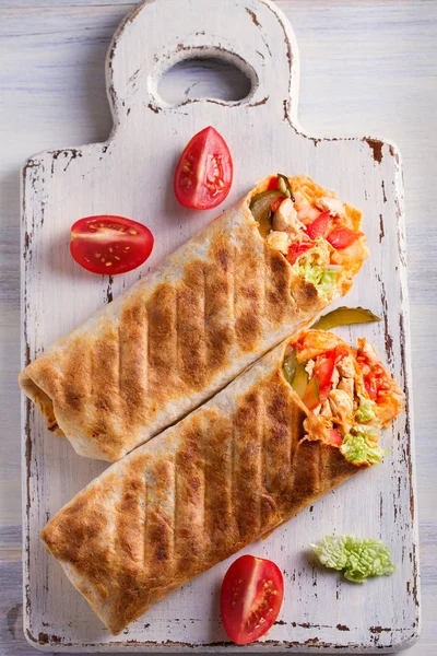 Chicken wraps with tomatoes, pickles, cabbage and onion on white chopping board and wooden table. Tortilla, burritos, sandwiches, twisted rolls