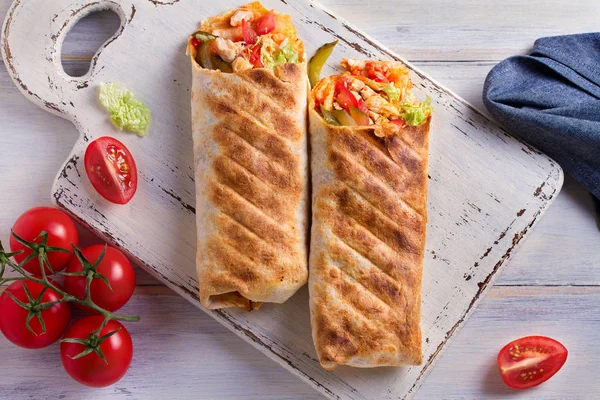 Tavuk domates, turşu, lahana ve soğan Beyaz Doğrama tahtası ve ahşap masa ile tamamladı. Tortilla, bükülmüş rulo börek, sandviç