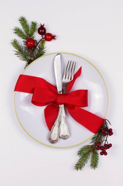 Tabak, çatal bıçak takımı, Çamın dalları, şerit ve beyaz masada kırmızı meyveler ile Noel kompozisyon. Kış tatili ve festival arka plan. Noel arifesi akşam yemeği, yılbaşı yiyecek öğle yemeği. üstten görünüm