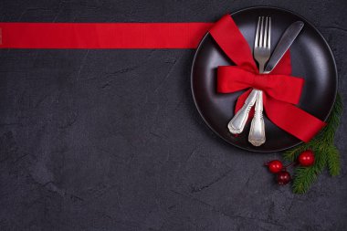 Tabak, çatal bıçak takımı, Çamın dalları, şerit ve siyah masada kırmızı meyveler ile Noel kompozisyon. Kış tatili ve festival arka plan. Noel arifesi akşam yemeği, yılbaşı yiyecek öğle yemeği. üstten görünüm
