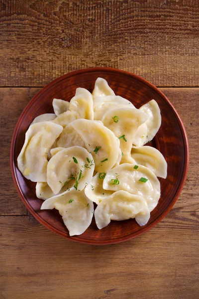 Dumplings, filled with mashed potato in plate on wooden table. Varenyky, vareniki, pierogi, pyrohy - dumplings with filling. Vegetarian dish. overhead, vertical