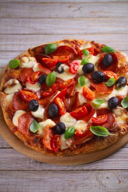  Biber, domates, peynir, zeytin ve fesleğen pizza. Güzel pizza ahşap rustik arka plan tabakta servis. dikey