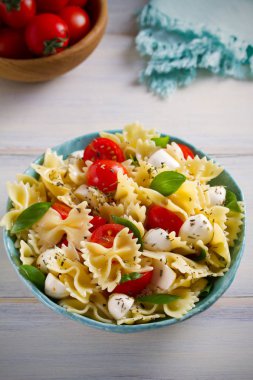 Caprese makarna salatası. Mozzarella peyniri, domates ve fesleğen ahşap masa üzerinde bir kapta makarna. dikey