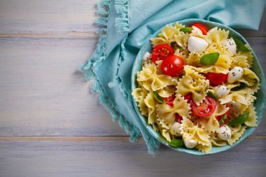 Caprese makarna salatası. Mozzarella peyniri, domates ve fesleğen ahşap masa üzerinde bir kapta makarna. Tepegöz, yatay 
