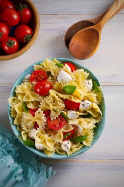 Caprese makarna salatası. Mozzarella peyniri, domates ve fesleğen ahşap masa üzerinde bir kapta makarna. Tepegöz, dikey 