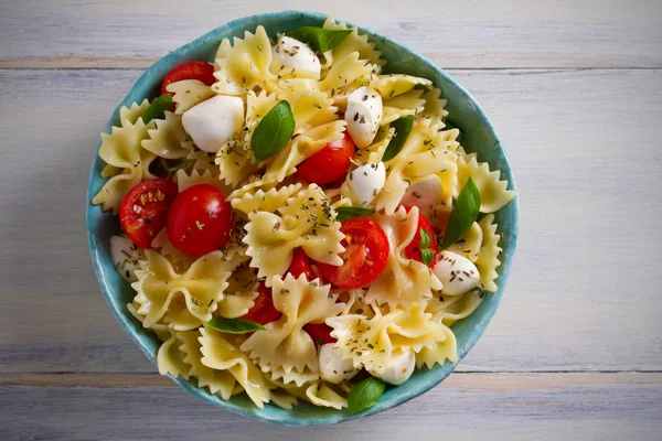 Caprese Pasta Salad. Pasta with mozzarella cheese, tomatoes and basil in bowl on wooden table. overhead, horizontal