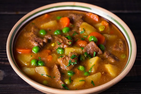 Homemade Irish beef stew with potatoes, carrots and peas in bowl on wooden table.  horizontal