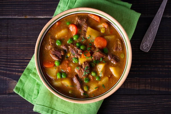 Homemade Irish beef stew with potatoes, carrots and peas in bowl on wooden table. overhead, horizontal