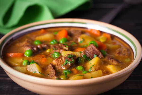 Homemade Irish beef stew with potatoes, carrots and peas in bowl on wooden table.  horizontal