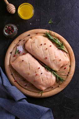 Çiğ çiğ kanatlı eti ahşap tepsi üzerinde kesti. Tatlım, biberiye ve baharatlar ile ördek göğsü