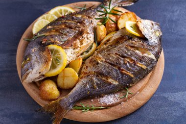 Ahşap tepsi üzerinde kavrulmuş patates, limon ve biberiye ile ızgara balık