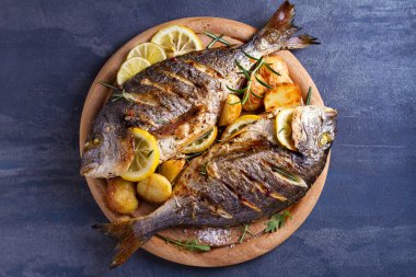 Kızarmış patates ile ızgara balık, ahşap tepsi üzerinde limon ve biberiye. Yukarıdan görünüm, üst