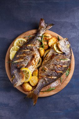 Kızarmış patates ile ızgara balık, ahşap tepsi üzerinde limon ve biberiye. Yukarıdan görünüm, üst