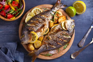 Kızarmış patates ile ızgara balık, ahşap tepsi üzerinde limon ve biberiye. Yukarıdan görünüm, üst