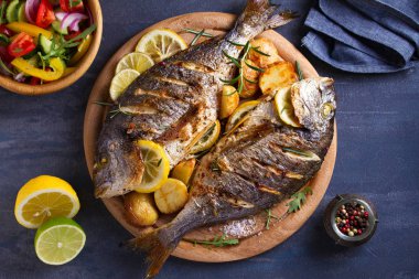 Kızarmış patates ile ızgara balık, ahşap tepsi üzerinde limon ve biberiye. Yukarıdan görünüm, üst