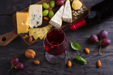 Siyah ahşap masada peynir, üzüm ve fındık ile cam ve şarap şişesi. Şarap ve yemek. Yukarıdan görüntüle, en iyi stüdyo çekimi