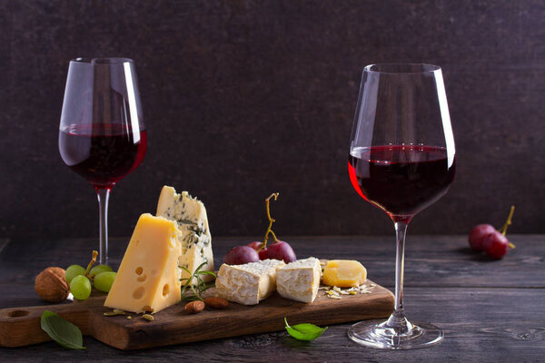 Glasses of wine with cheese, grapes, and nuts on black wooden table. Wine and food
