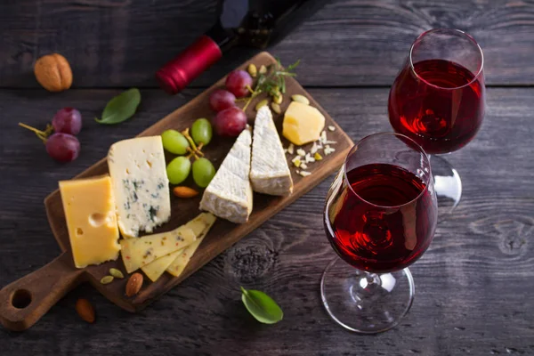 黒い木製のテーブルの上にチーズ ブドウ ナッツを入れたグラスとワインのボトル ワインと食べ物上からの眺め トップスタジオショット — ストック写真