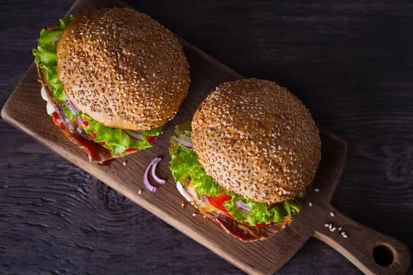 Delicious homemade beef burgers with bacon on wooden chopping board. overhead, horizontal
