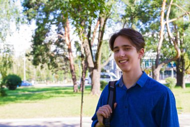 Bir omuz ve gülümseyen bir öğrenci sırt çantası taşıyan. Parkta dış portre. Çalışmaya hazır