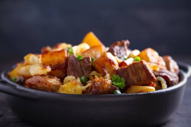 Soğan ve sarımsak ile kızarmış sığır eti ve patates ahşap arka plan üzerinde siyah çanak servis