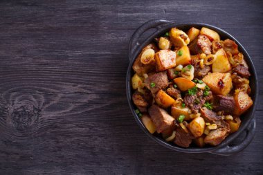 Soğan ve sarımsak ile kızarmış sığır eti ve patates ahşap arka plan üzerinde siyah çanak servis edilir. Kopya alanı, metin için oda