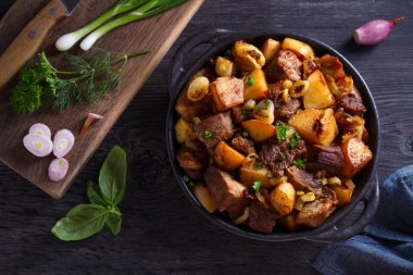 Soğan ve sarımsak ile kızarmış sığır eti ve patates ahşap arka plan üzerinde siyah çanak servis